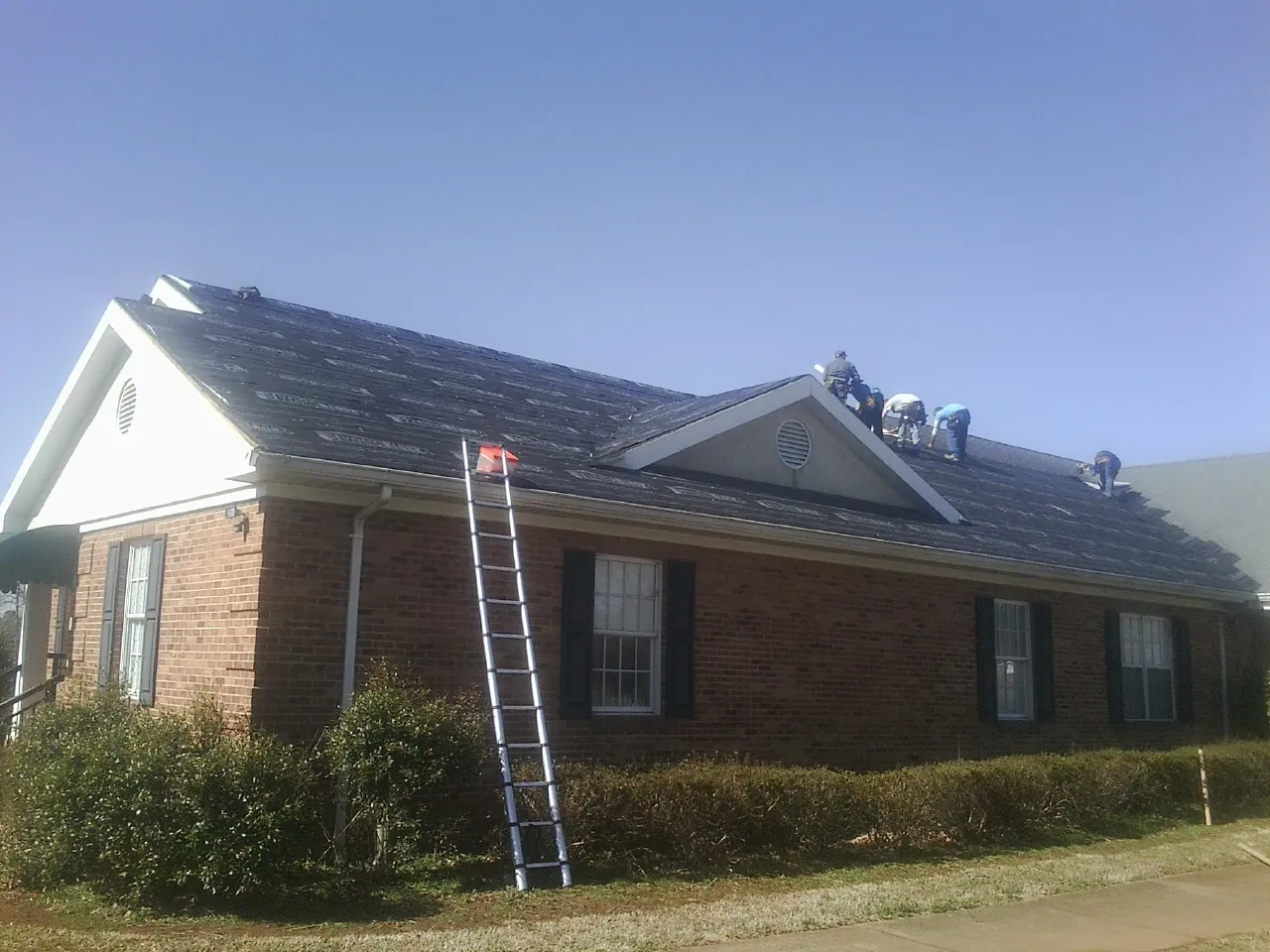 Crew tearing shingles off a brick ranch roof with a ladder set — Emergency Roof Repair work by our crew in Norway
