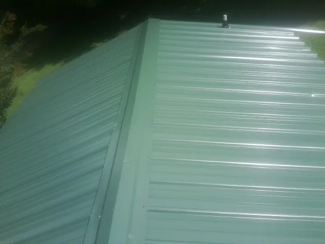 New green metal panels meeting at the ridge of a roof — Flat Roof Repair work by our crew in Norway